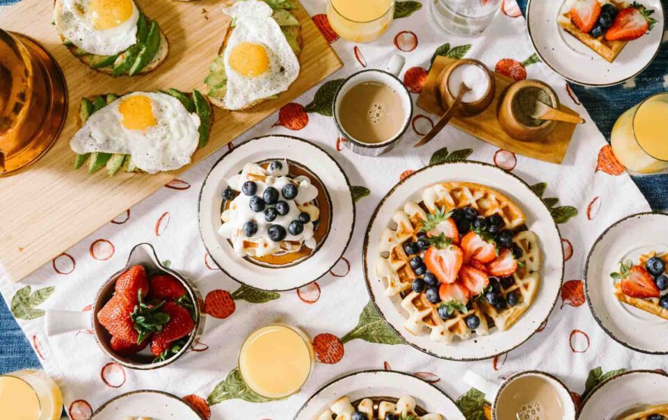 Table filled with different breakfast foods for like waffles, avocados and eggs an strawberries