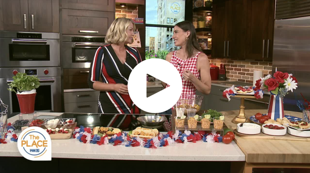 Two women standing in front of a counter with 4th of July food. 